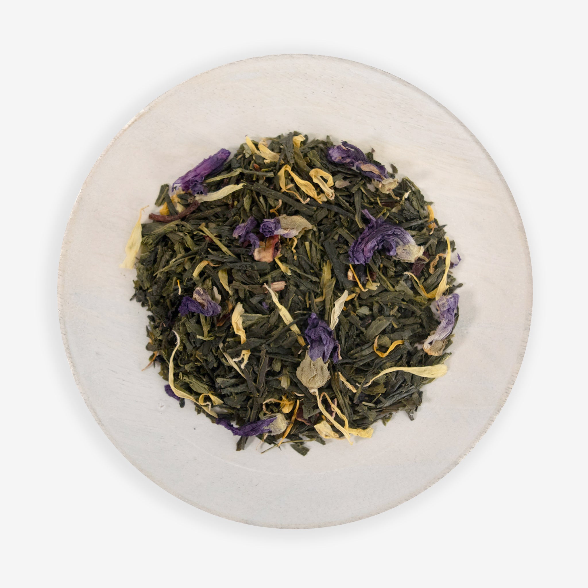 A top view of a plate containing dried tea leaves and pieces of hibiscus flowers, with hints of purple and yellow, on a white background.