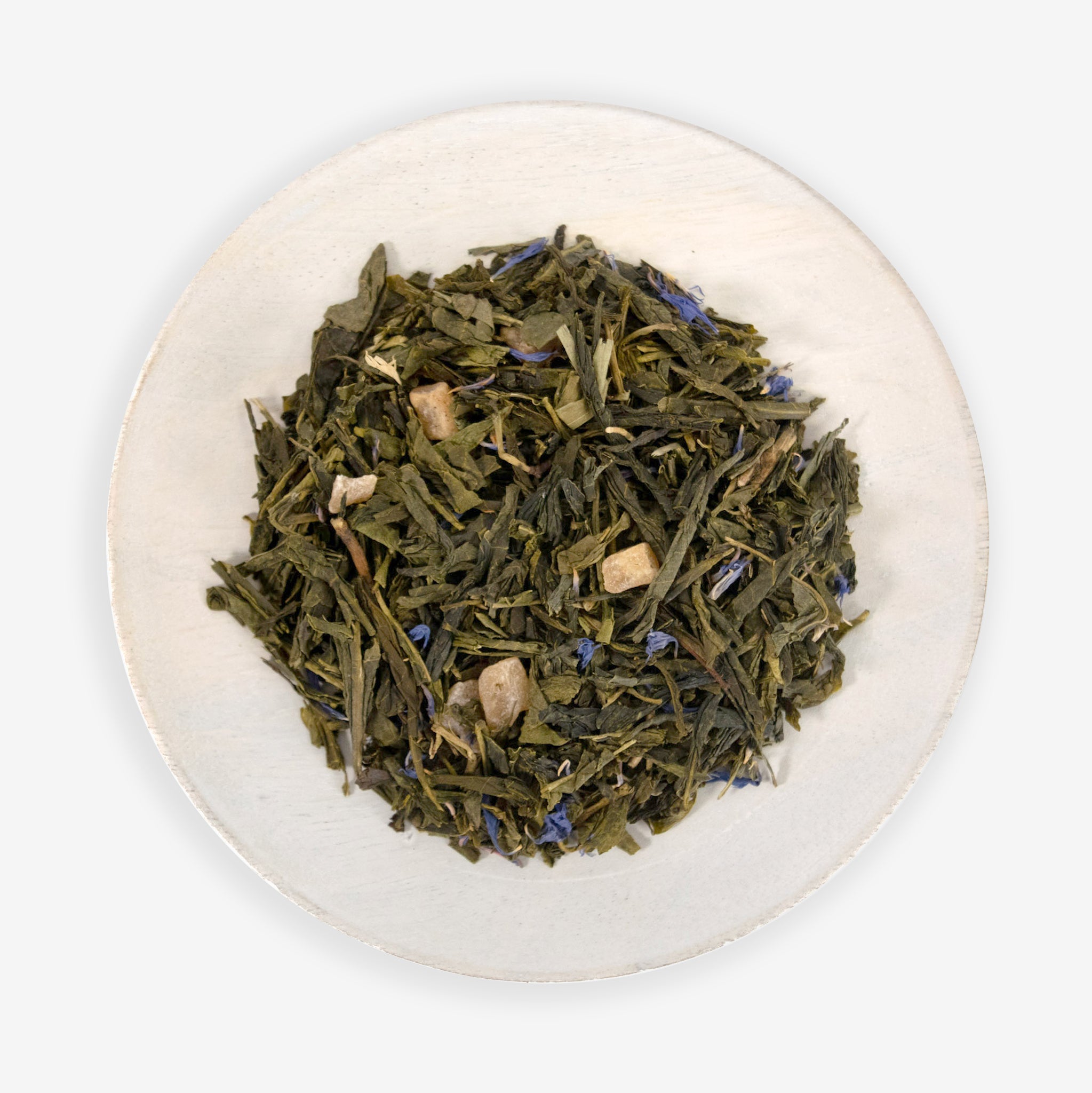 A dish containing green tea leaves, air-dried mango pieces, and blue cornflower petals, indicative of the ingredients in the tea product &