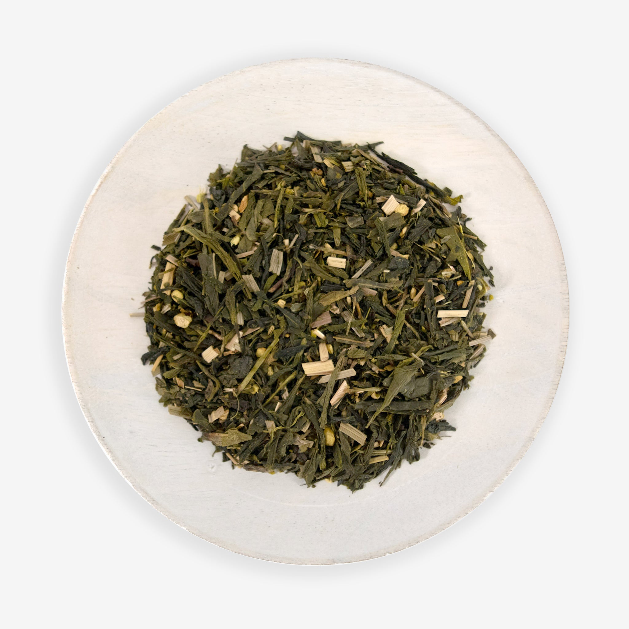 A top view of a plate containing loose leaf green tea mixed with pieces of ginger and lemongrass.