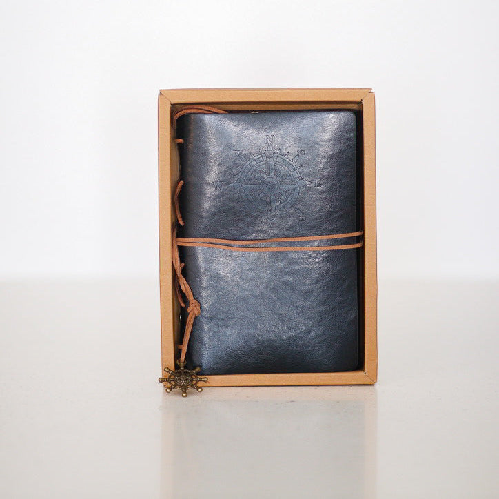Blue leather-bound notebook with brown strap in a cardboard box on a white background