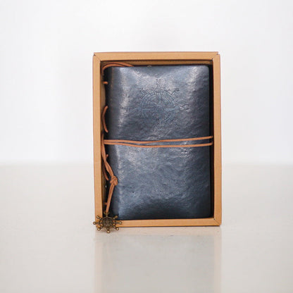 Blue leather-bound notebook with brown strap in a cardboard box on a white background