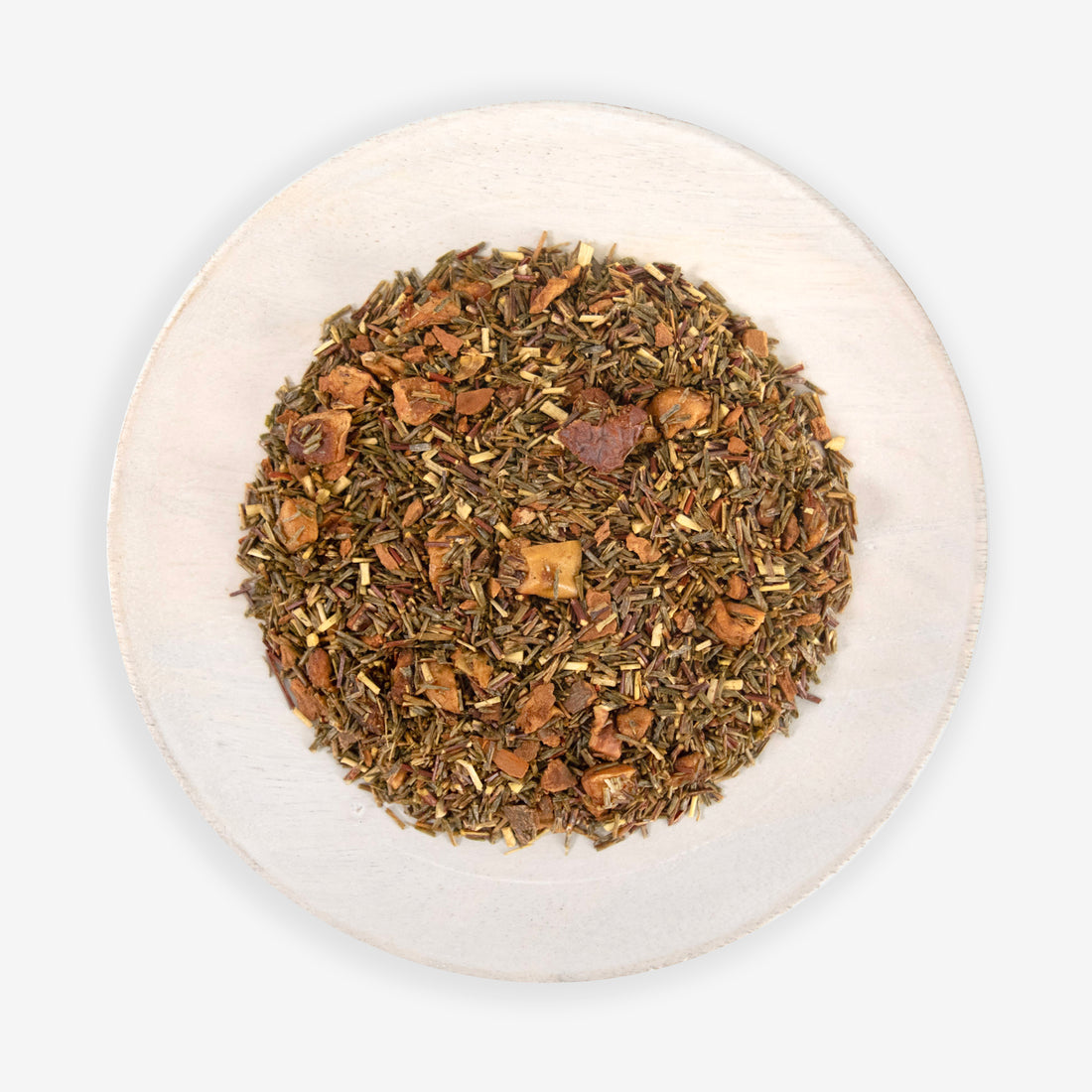 A top view of a plate containing Homemade Apple Cider tea leaves, which include South African green rooibos, cinnamon pieces, and air-dried apple pieces.